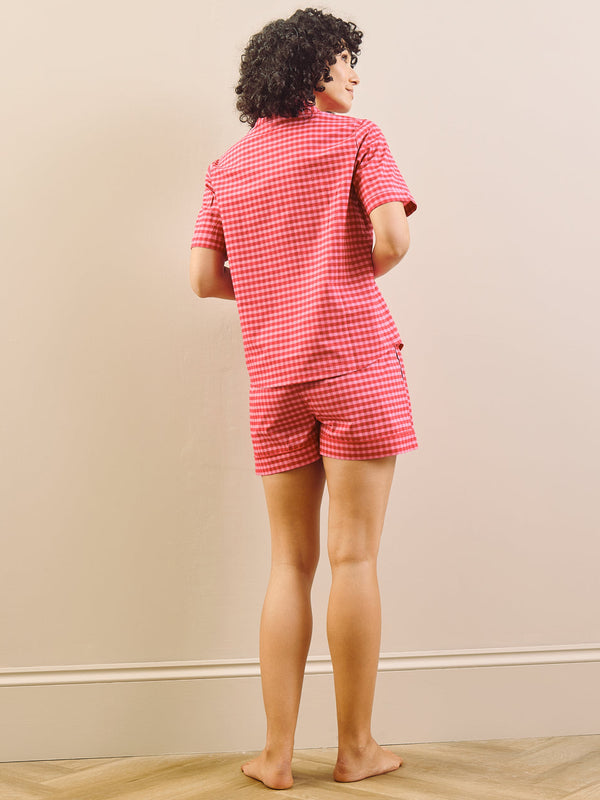 Person wearing a red gingham pyjama set standing in a room with a beige wall. Back