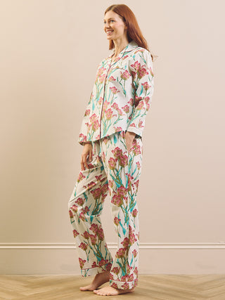 A woman modelling a matching pyjama set with a floral print, standing barefoot against a neutral beige wall and light wood floor.