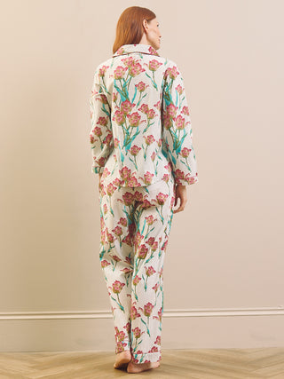 A woman stands barefoot in a room wearing a matching pyjama set from the back. The pajamas are off-white with a pink and green floral print.