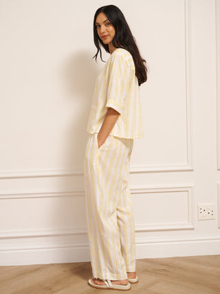 Woman wearing a yellow and white striped linen blend co-ord set with V-neck top and loose trousers. Side View