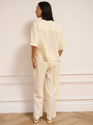 Woman wearing a yellow and white striped linen blend co-ord set with V-neck top and loose trousers. Back view