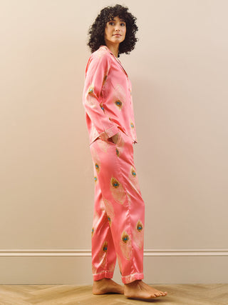 Person wearing pink pyjamas with a peacock feather pattern in a room with a beige wall and wooden floor.