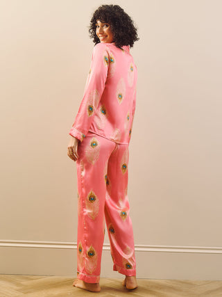 Woman wearing pink pyjamas with a peacock feather pattern in a room with a beige wall and wooden floor.