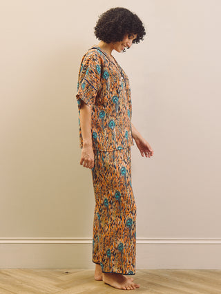 Woman wearing a patterned feather print pyjama set standing against a plain wall.
