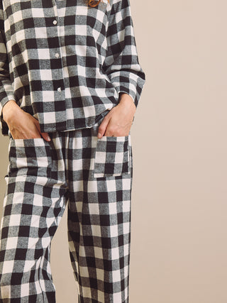 A person wearing a black and white gingham check long-sleeve pyjama set with a button-front top and matching pants, standing against a plain beige background.