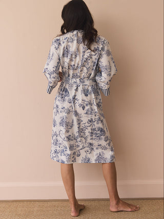 Woman wearing a toile floral dressing gown robe against a beige wall.