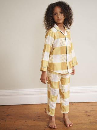 Child wearing yellow and white checkered pyjamas standing on a wooden floor.