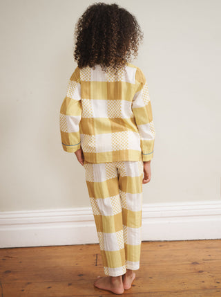 Child wearing yellow and white checkered pyjamas standing on a wooden floor. Back Detail. 