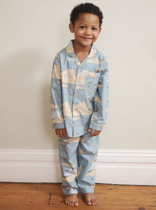 Child wearing a blue clouds patterned pyjama set standing on a wooden floor against a white wall.