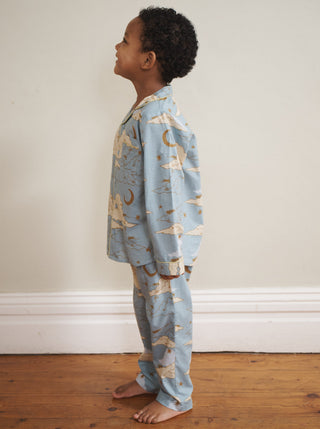Child wearing blue pyjamas with cloud and moon print standing on a wooden floor.