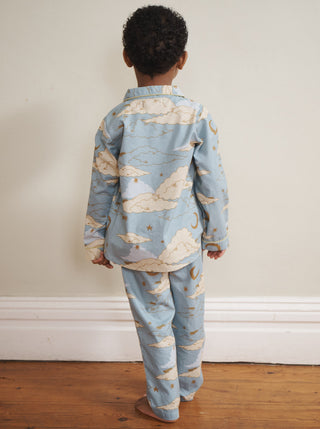 Child wearing a blue and white cloud-patterned pyjama set standing on a wooden floor.