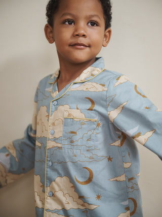 Child wearing a blue moon and cloud print pyjama set with celestial pattern on a neutral background