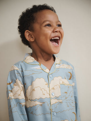 Child wearing pyjamas with cloud and moon patterns, laughing against a plain background