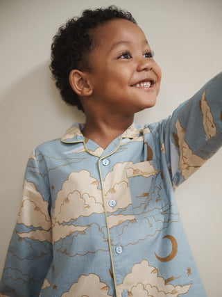 Child wearing a blue pyjama set with cloud and moon pattern against a plain background