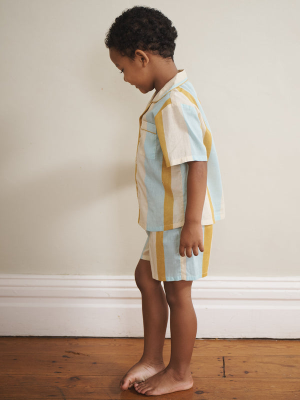 Child wearing a colourful striped pyjama set standing against a plain wall.