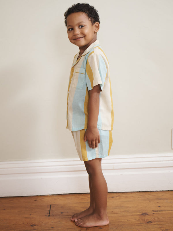 Child wearing colorful pyjamas standing on a wooden floor against a white wall.