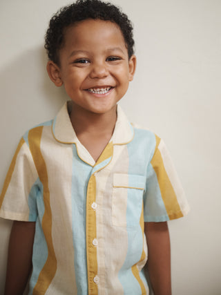 Child wearing a colourful striped pyjama  shirt against a plain background