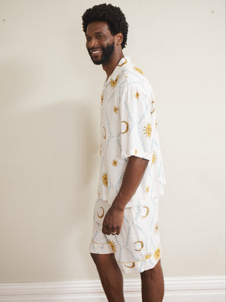 Man wearing cream short pyjama set with celestial pattern against a plain background