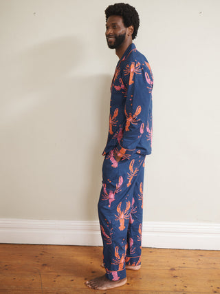 Person wearing a blue pyjama set with pink lobster pattern standing against a white wall.
