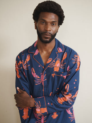 Man wearing a navy blue pyjama set with pink lobster pattern against a plain background