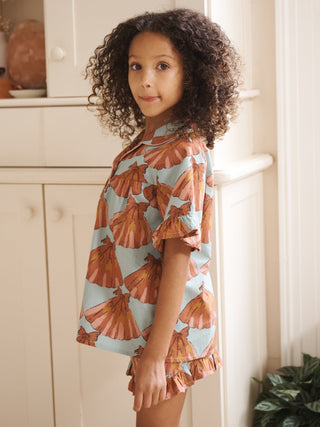 Young girl wearing a short pyjama set outfit standing in a room with white cabinets and plants.
