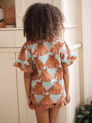 Child wearing a shell-patterned pyjama set standing in a room with a cabinet and window.