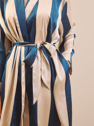 A close-up of a person wearing a long-sleeve wrap-style robe or kimono with bold vertical stripes in deep blue and warm cream, tied at the waist with a matching fabric belt.