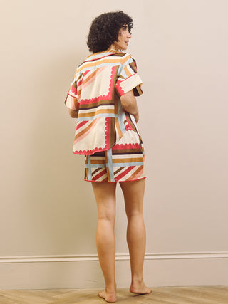 Woman wearing a colourful patterned short pyjama set against a beige background