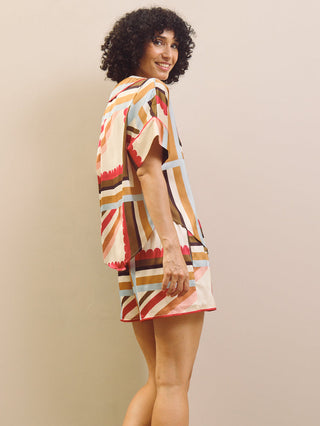 Woman wearing a colourful patterned short pyjama set against a beige background