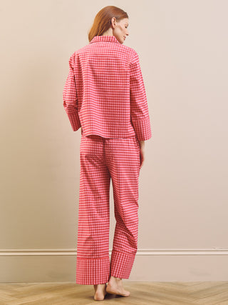 Model wears pinking gingham boxy pyjama set against a beige nurtural wall. Back view.