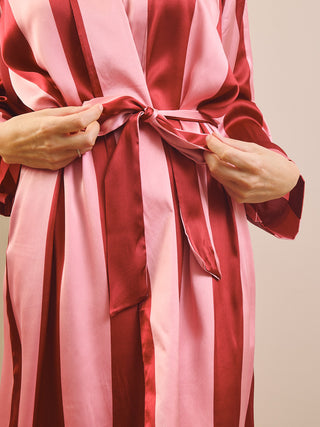 A close-up of a person wearing a silky robe with vertical stripes in pink and deep red, tying the waist tie with both hands.