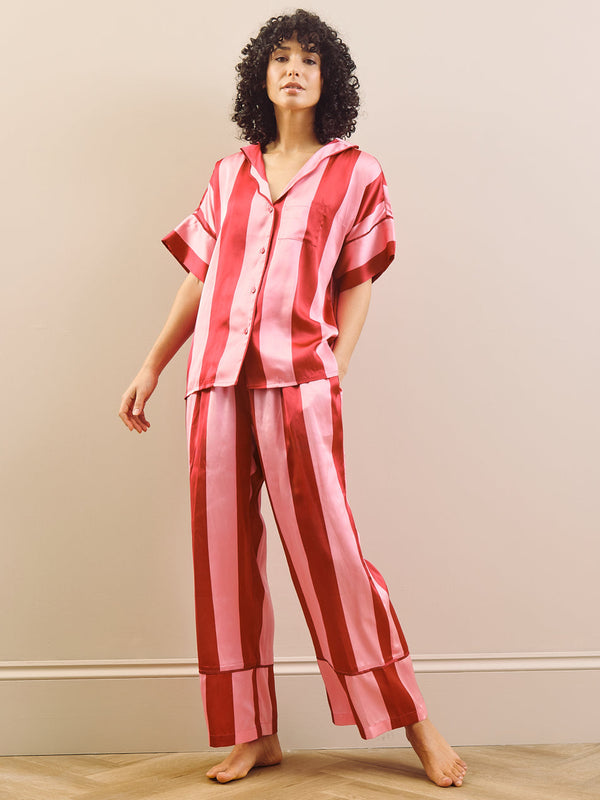 Woman wearing a pink and white striped pyjama set against a plain wall.