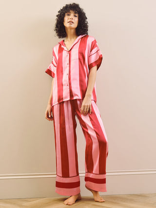Model wearing a pink striped long pyjama set standing against a plain wall.