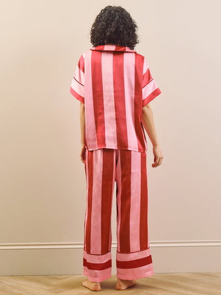Model wearing a pink striped long pyjama set standing against a plain wall. Back detail.