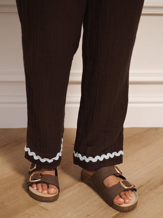 Brown pants with white trim worn by a person on a wooden floor.