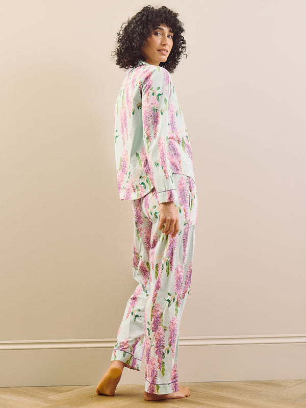 model wears long wisteria print pyjamas on beige background, back