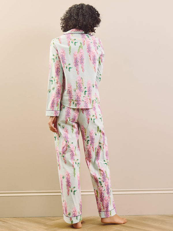 model wears long wisteria print pyjamas on beige background, back