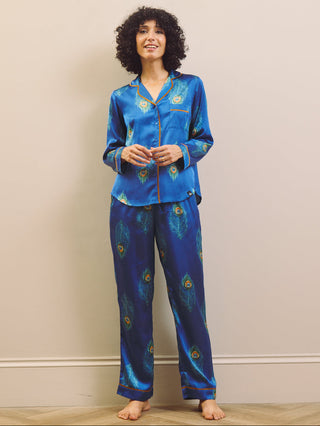 Woman wearing a blue satin pajama set with peacock feather design against a plain background