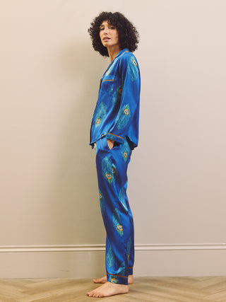 Person wearing a blue satin pajama set with peacock patterns on a beige background