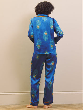 Person wearing blue pajama set with peacock feather pattern on a beige wall background