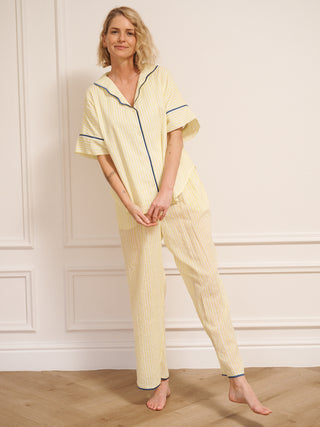Model wearing a yellow pyjama set with blue piping against a white wall.