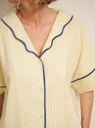 Model wearing a yellow pyjama set with blue piping against a white wall. detail
