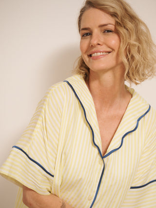 Model wearing a yellow pyjama set with blue piping against a white wall.