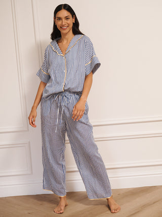 Model wearing women’s navy ticking stripe cotton gauze pyjamas with short-sleeved button-up top, drawstring waist trousers and contrast trim, photographed in a neutral studio setting.