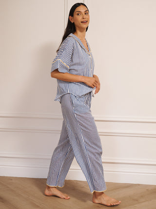 Model wearing women’s navy ticking stripe cotton gauze pyjamas with short-sleeved button-up top, drawstring waist trousers and contrast trim, photographed in a neutral studio setting. Side detail,