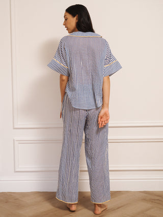 Model wearing women’s navy ticking stripe cotton gauze pyjamas with short-sleeved button-up top, drawstring waist trousers and contrast trim, photographed in a neutral studio setting. Back detail