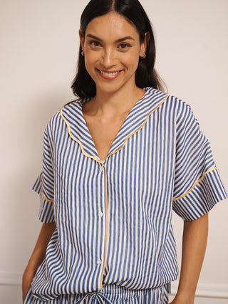 Model wearing women’s navy ticking stripe cotton gauze pyjamas with short-sleeved button-up top, drawstring waist trousers and contrast trim, photographed in a neutral studio setting.