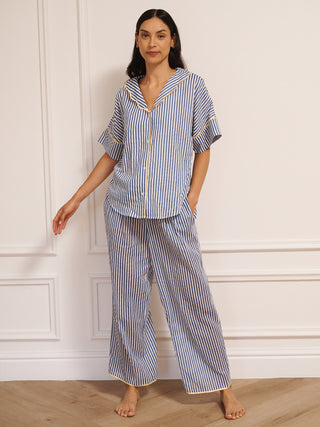 Model wearing women’s navy ticking stripe cotton gauze pyjamas with short-sleeved button-up top, drawstring waist trousers and contrast trim, photographed in a neutral studio setting.