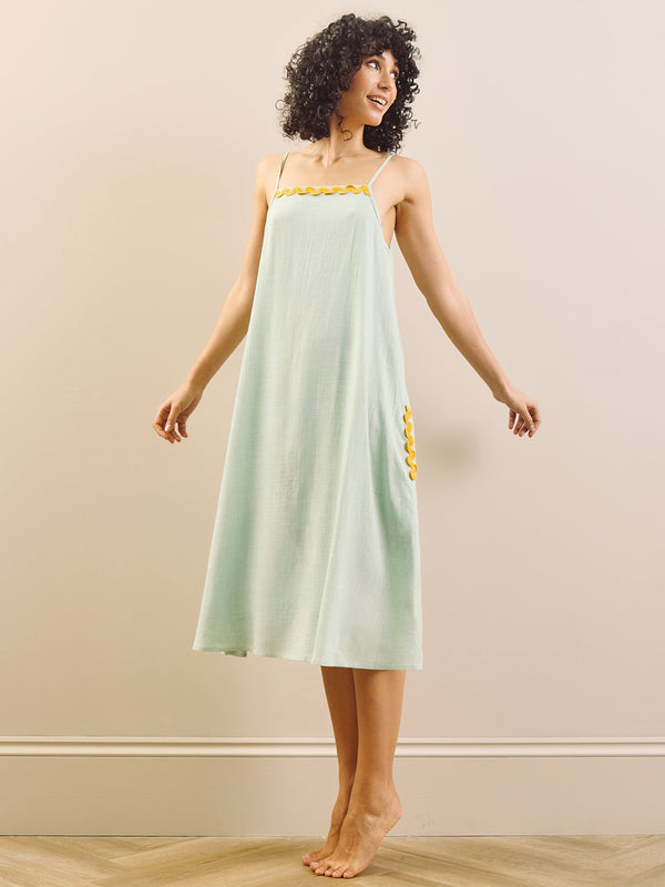 model wears linen blend nightie with contrast trim against a beige wall. 