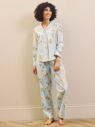 Woman wearing a light blue floral pyjama set against a beige wall.